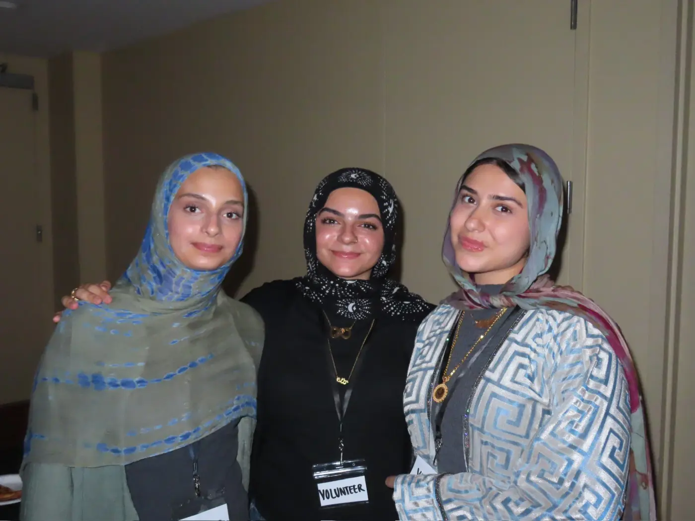 Three volunteers in hijabs posing together, one wearing a volunteer badge