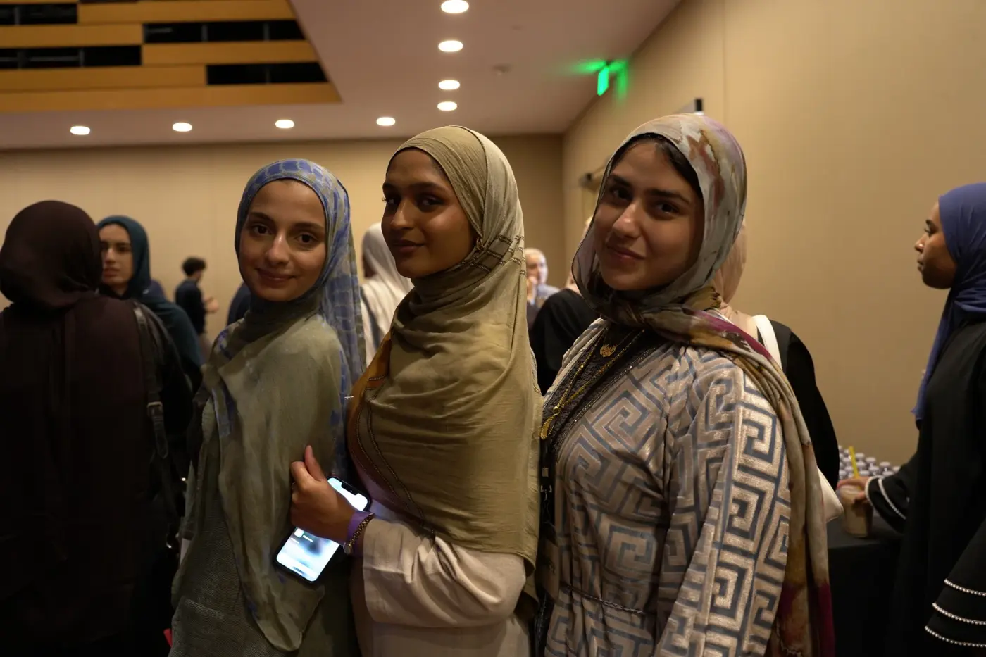 Attendees in hijabs smiling at the camera in a lobby crowd