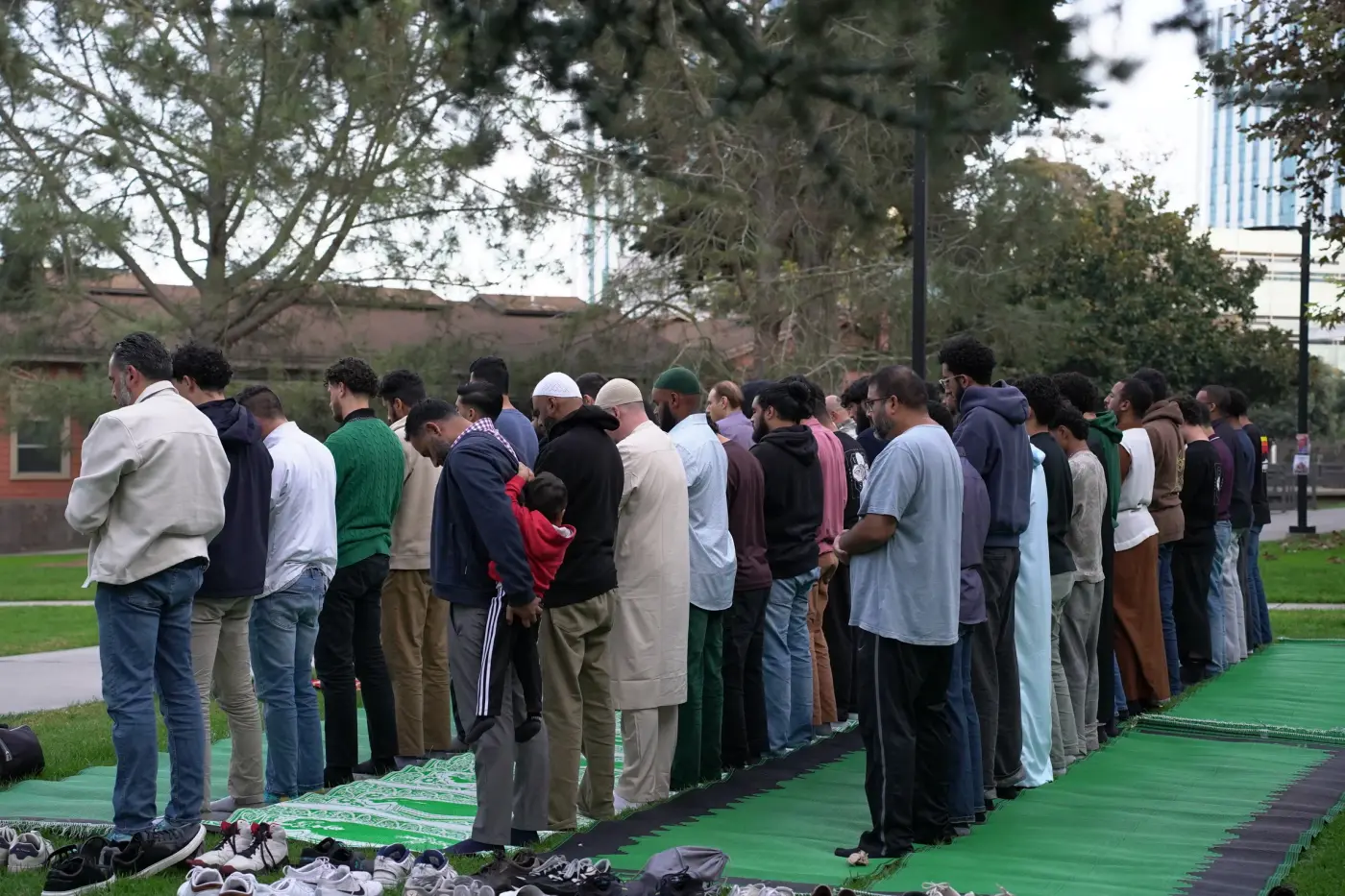 Rows of attendees praying together on green mats on the lawn